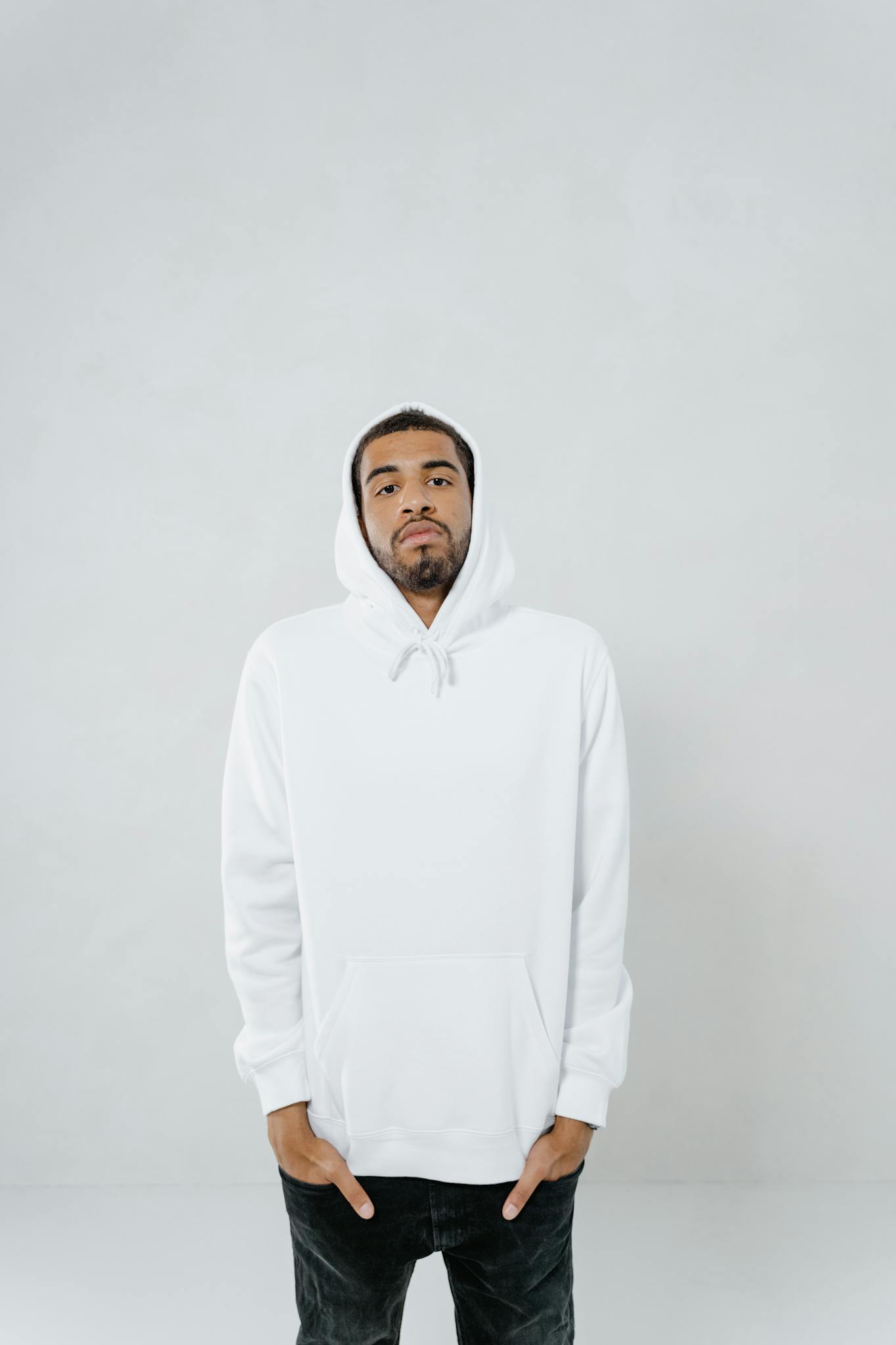 Portrait of a man wearing a white hoodie with hands in pockets against a neutral background.