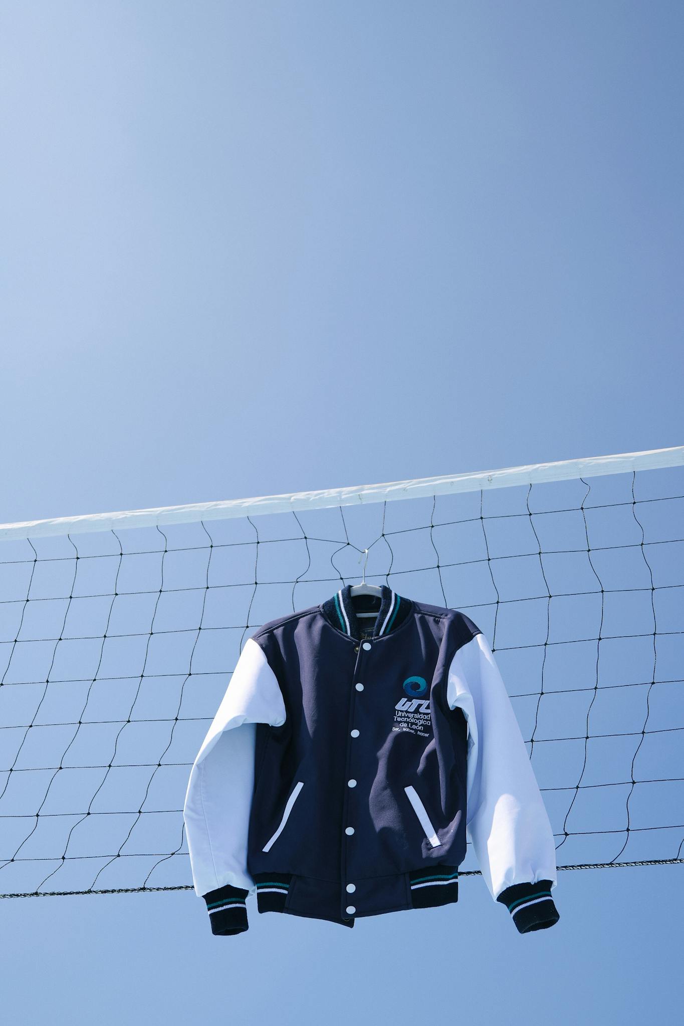 Varsity jacket draped over a soccer net against a clear blue sky in León, Mexico.