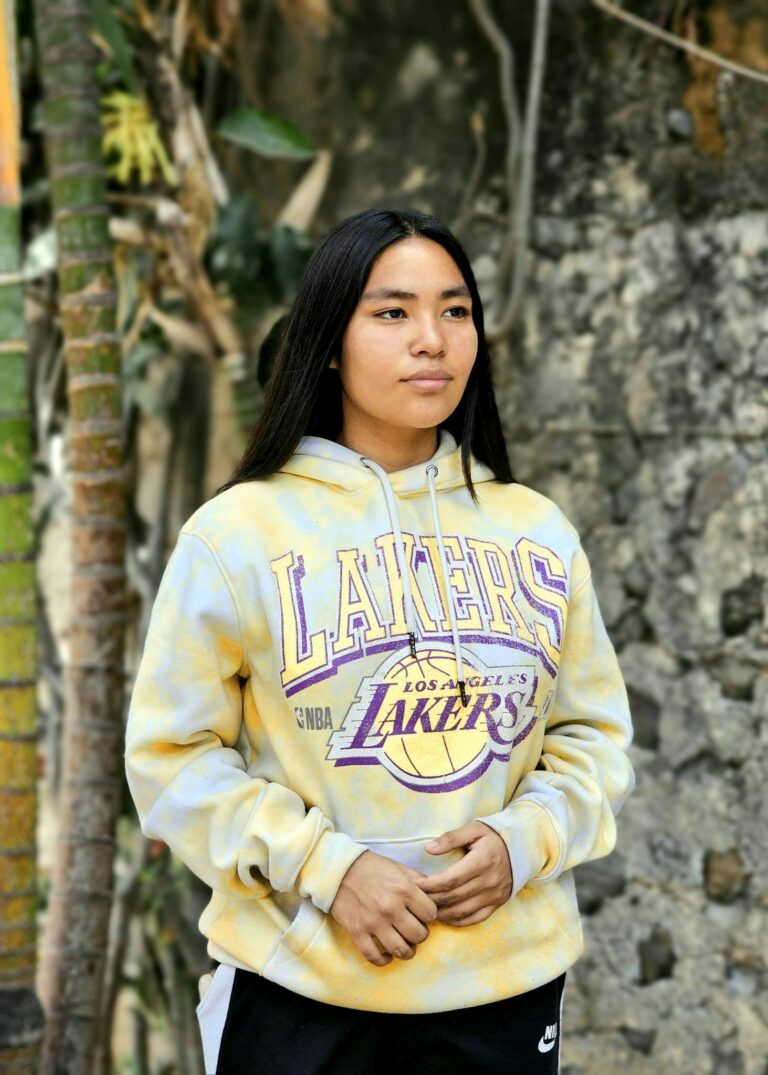 Young adult in a Lakers hoodie stands outdoors with a focused expression.